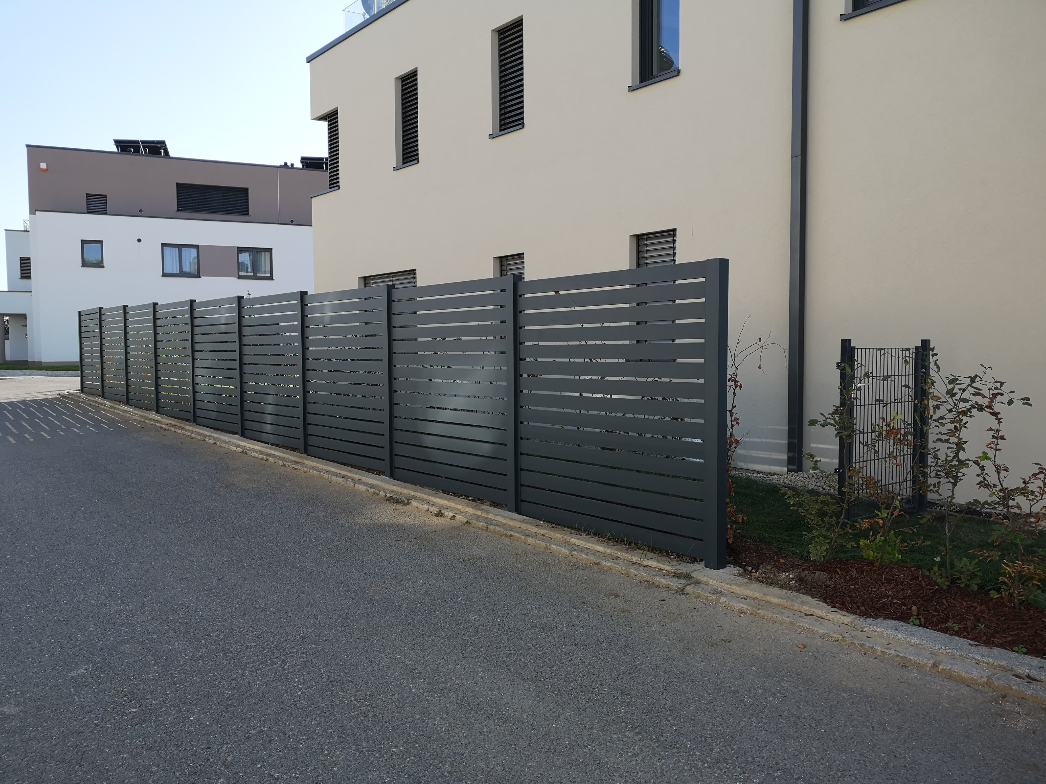 Clôture aluminium à lames anthracite le long d'une voie d'accès, réalisation Green Space