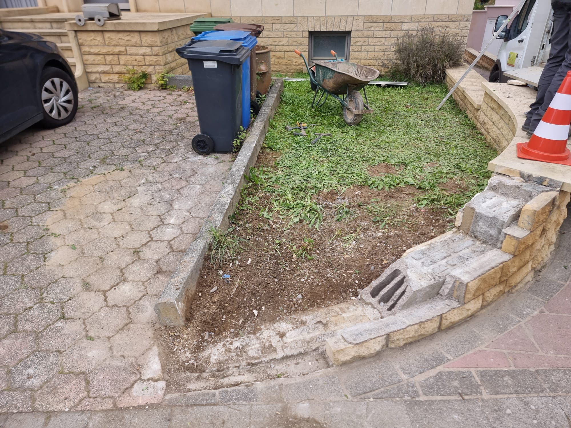 Parterre en terre et herbe folle devant une maison en pierre, mur de soutènement en cours